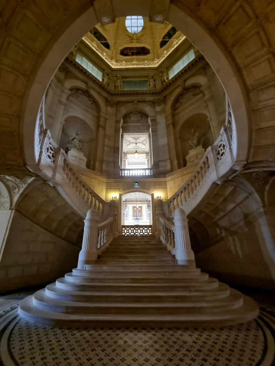 Un grand escalier de pierre sous une coupole dorée dans un palais de justice à Paris