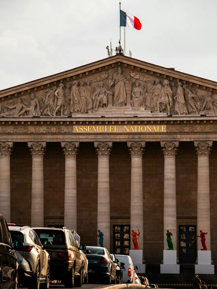 Façade du Palais Bourbon, siège de l'Assemblée nationale, à Paris, surmontée d'un drapeau français.