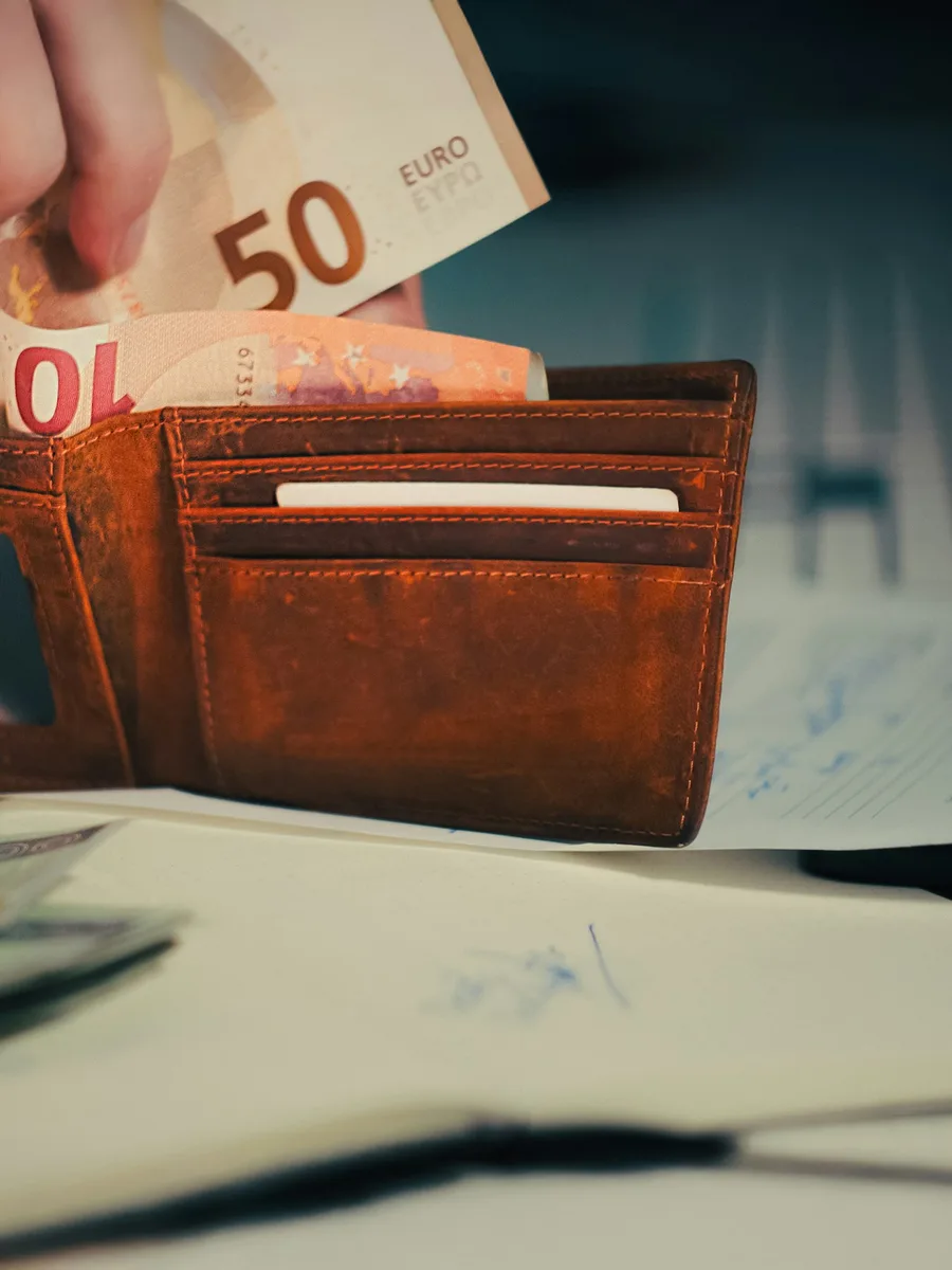 Une main glisse des billets en euros, dont un billet de 50 euros, dans un portefeuille en cuir usé