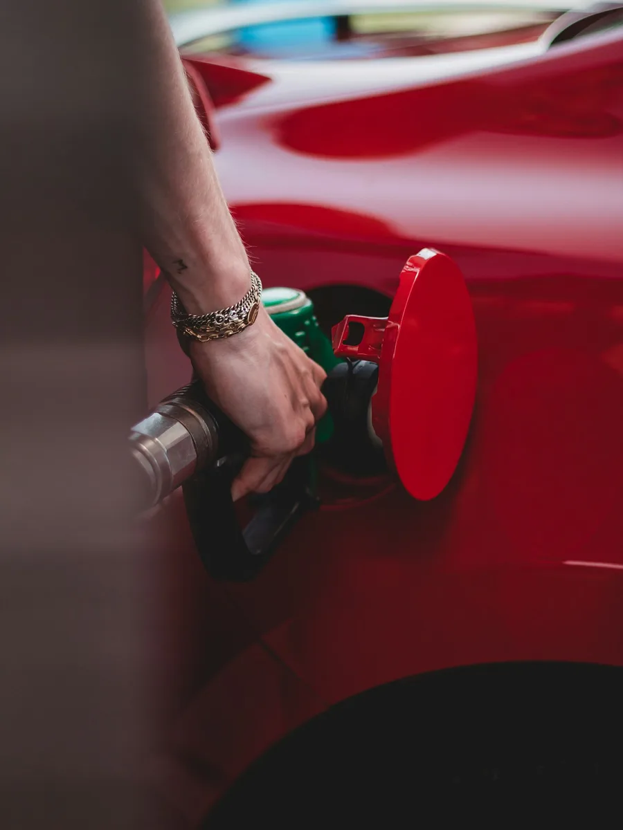 Une main tient un pistolet de pompe à essence branché sur le réservoir d'une voiture rouge