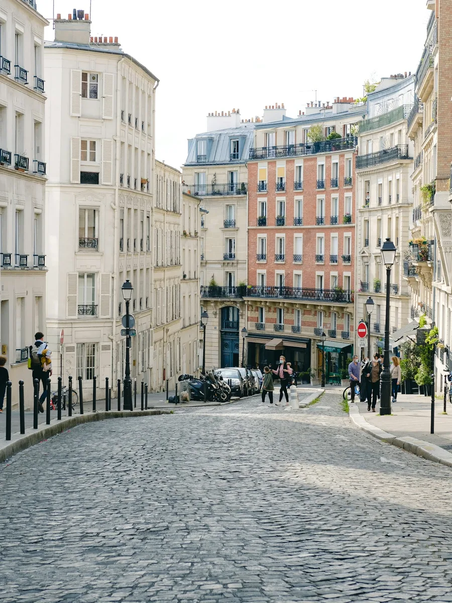 Une rue pavée de Montmartre, à Paris, bordée d'immeubles, avec quelques passants au loin