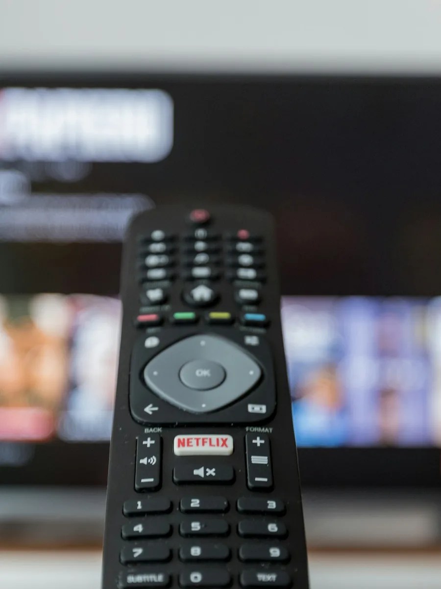 Une télécommande posée sur une table devant un téléviseur allumé