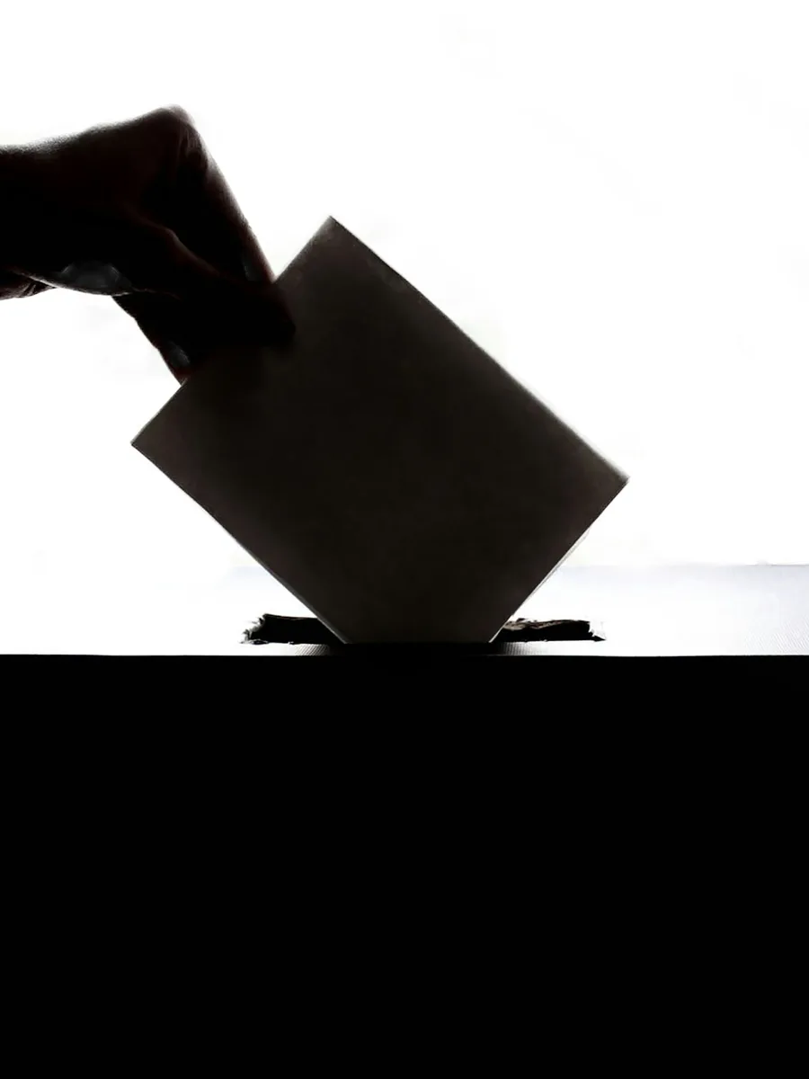 Silhouette d'une main glissant une enveloppe dans une urne