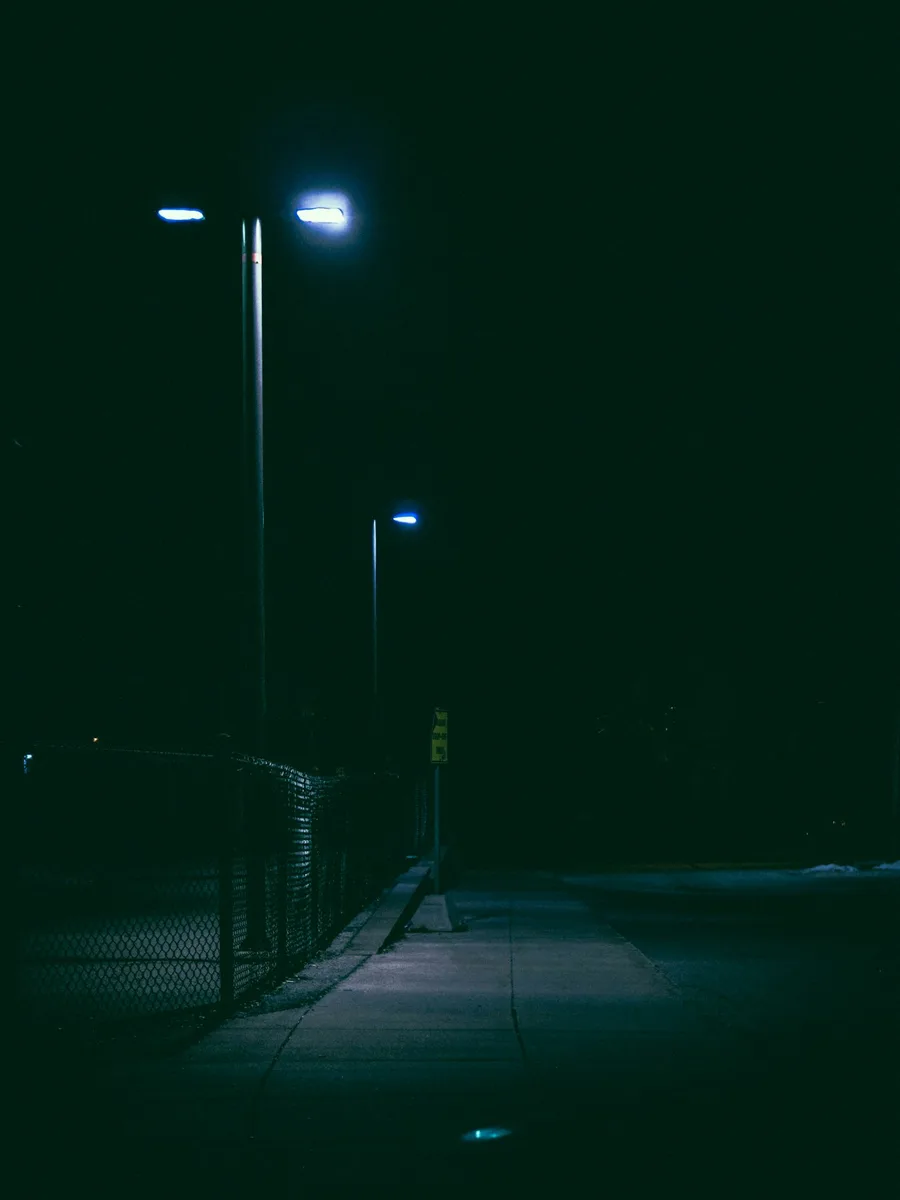 Un lampadaire allumé dans l'obscurité, au bord d'une route déserte.