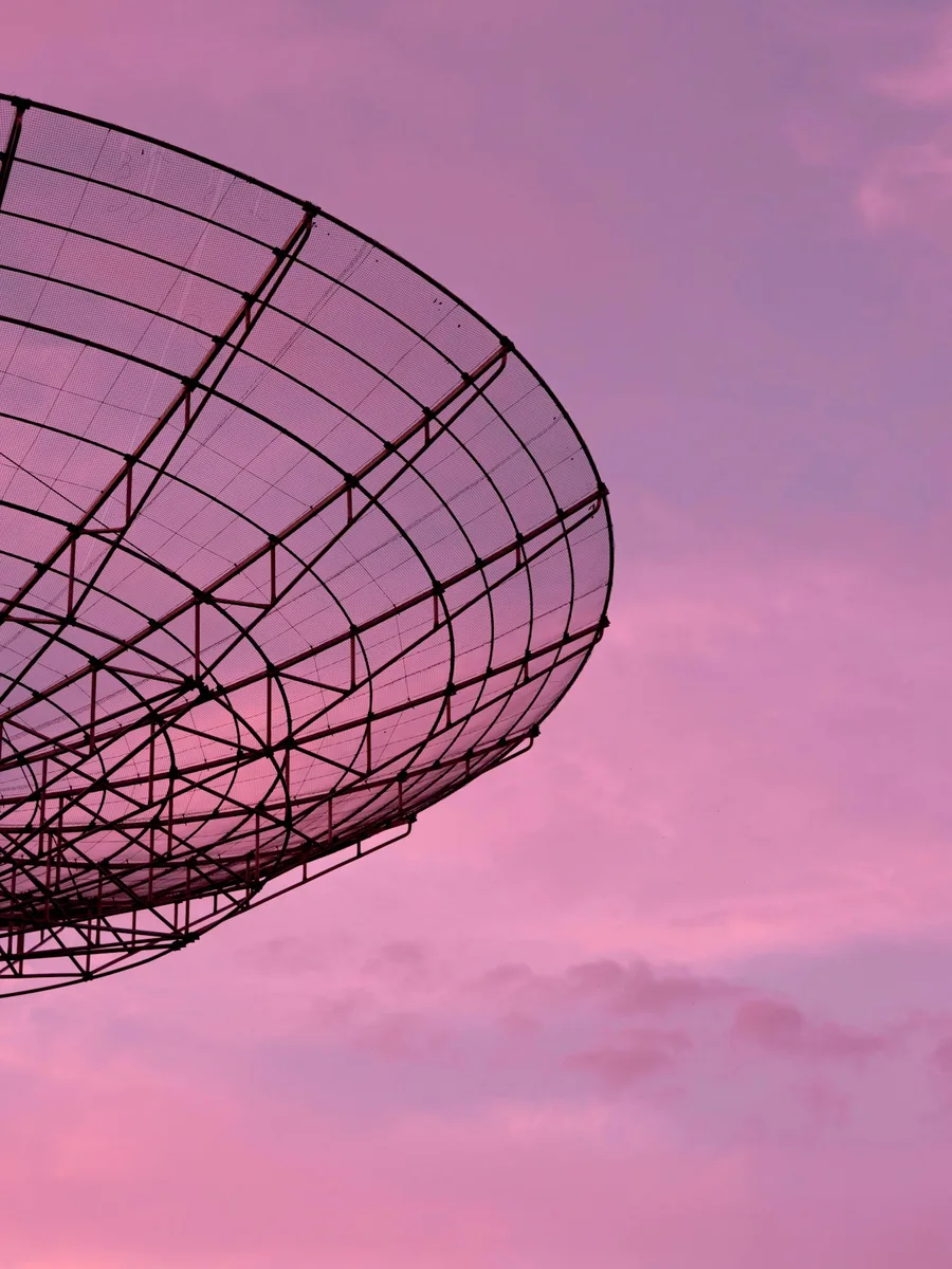 La silhouette d'une antenne parabolique en treillis métallique sur un ciel rose