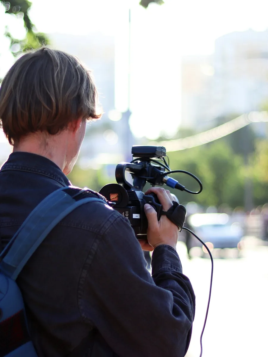 Une personne de dos filme avec une caméra professionnelle en extérieur