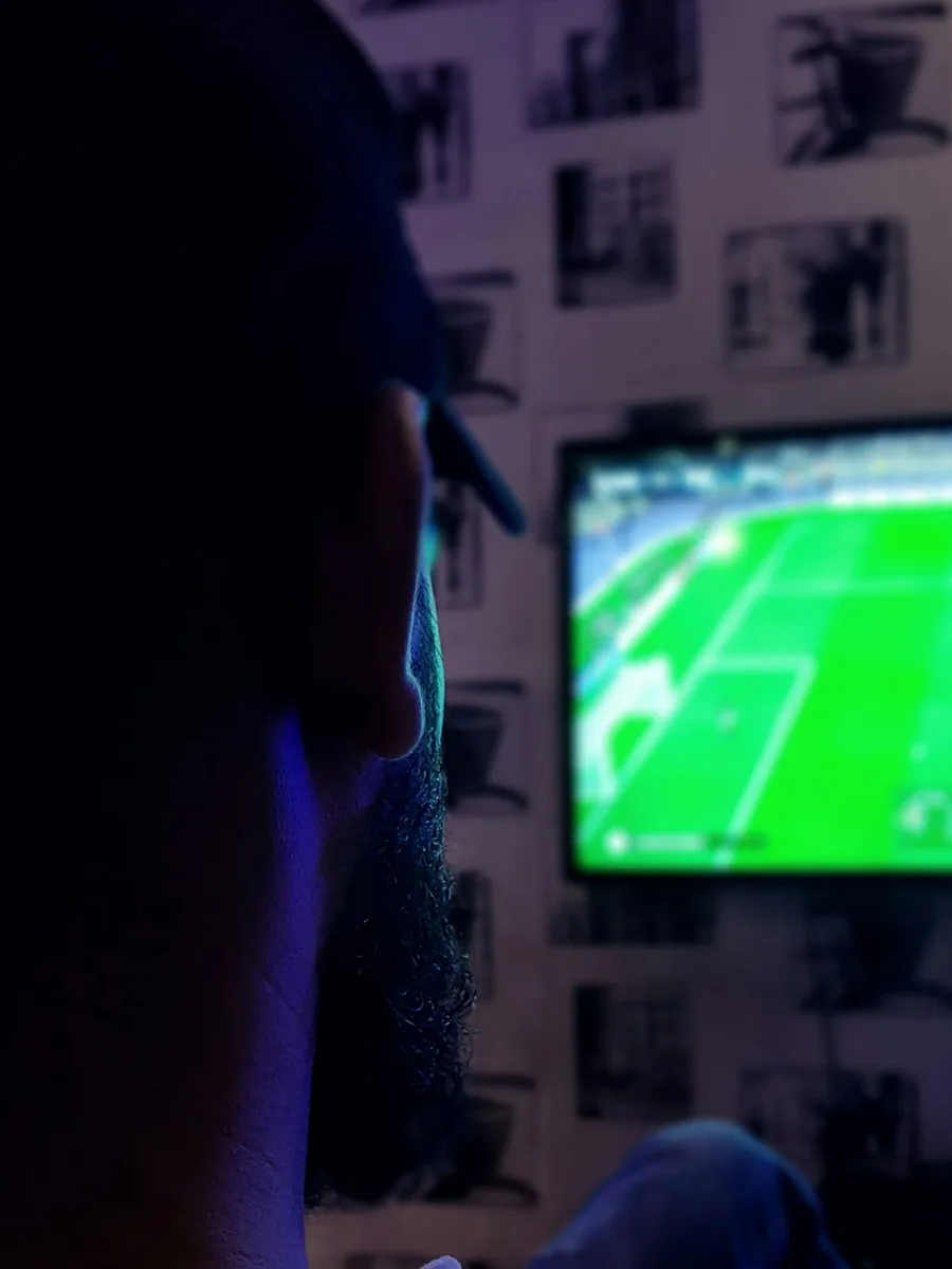Un spectateur dans la pénombre devant un écran qui diffuse un match de football