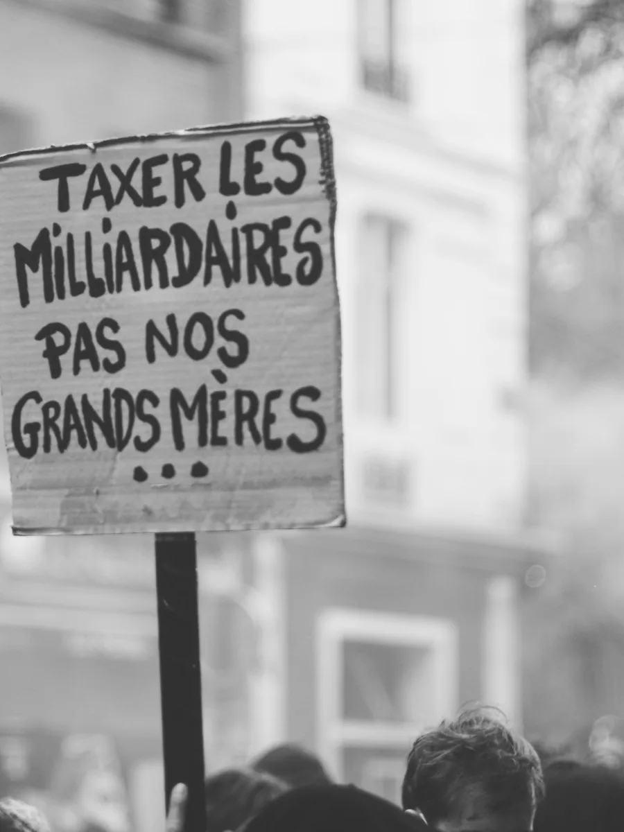 Une pancarte « Taxer les milliardaires, pas nos grands-mères » brandie dans une manifestation, en noir et blanc