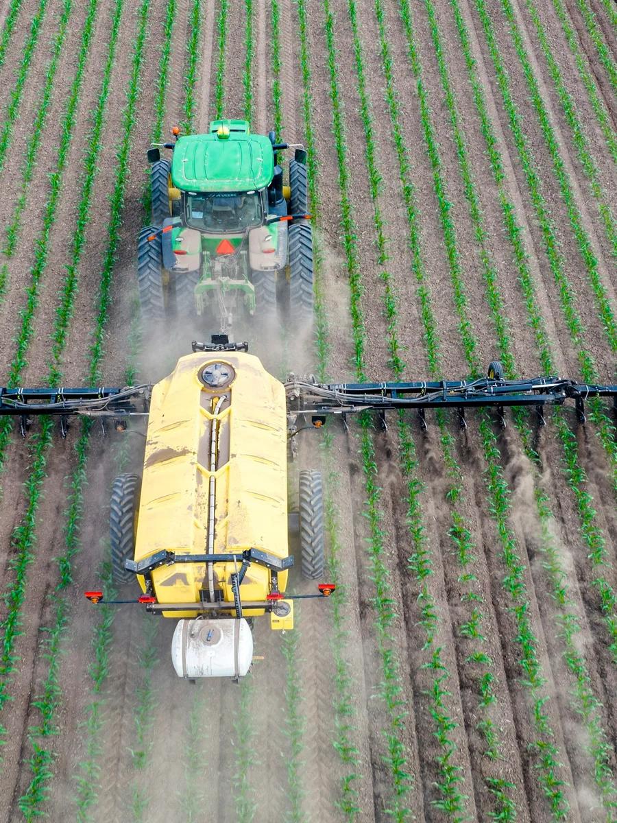 Vu du ciel, un tracteur tire un pulvérisateur entre des rangs de cultures