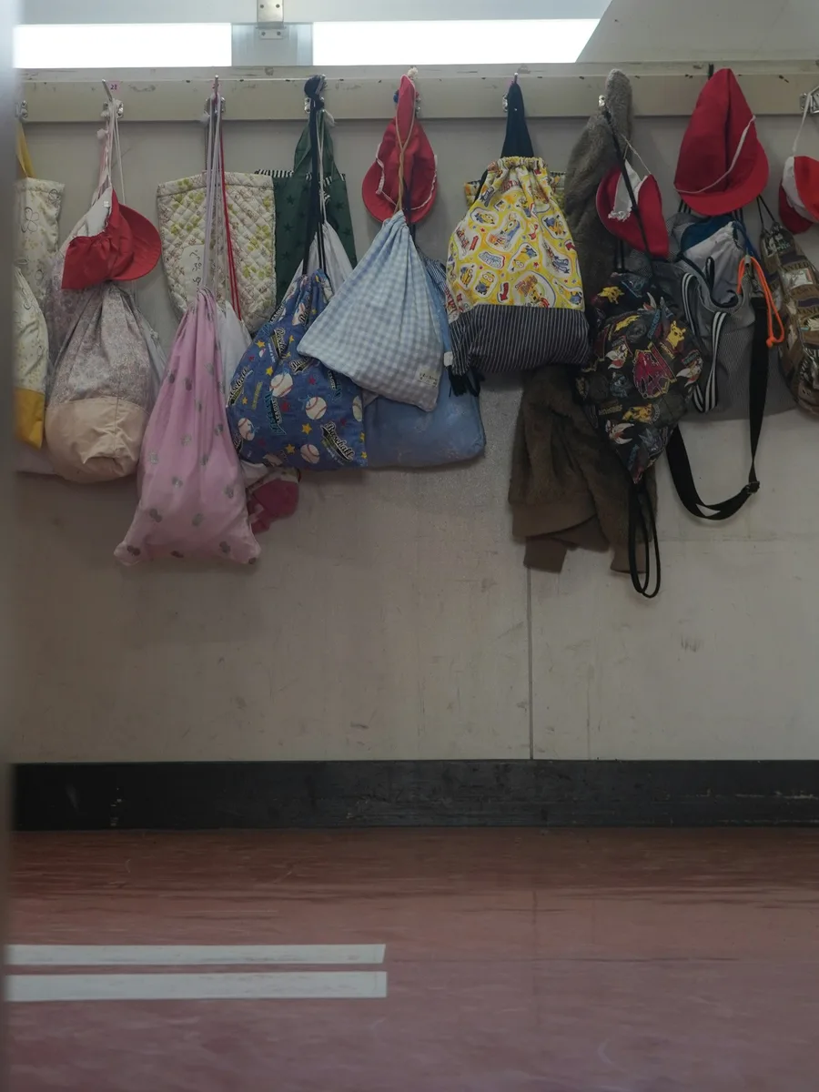 Sacs en tissu colorés et chapeaux d’enfants accrochés à des patères le long du mur d’un couloir d’école