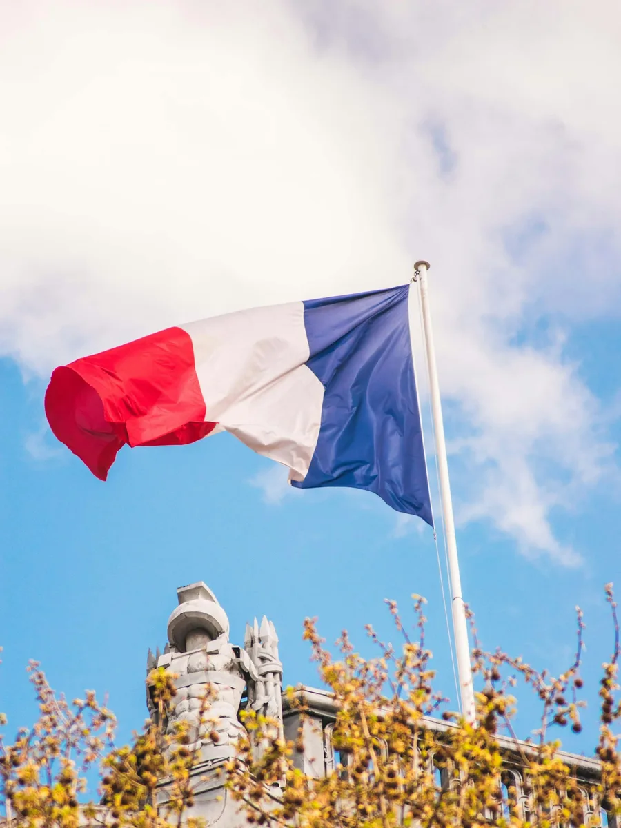 Un drapeau français flotte au sommet d'un mât sous un ciel nuageux