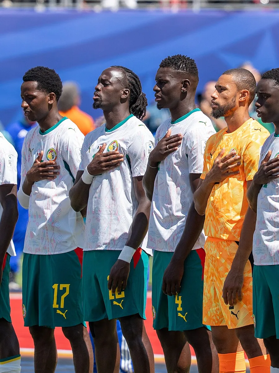 Joueurs de l’équipe du Sénégal en maillot blanc et short vert, alignés main sur le cœur pendant l’hymne, avec le gardien en tenue orange au centre.
