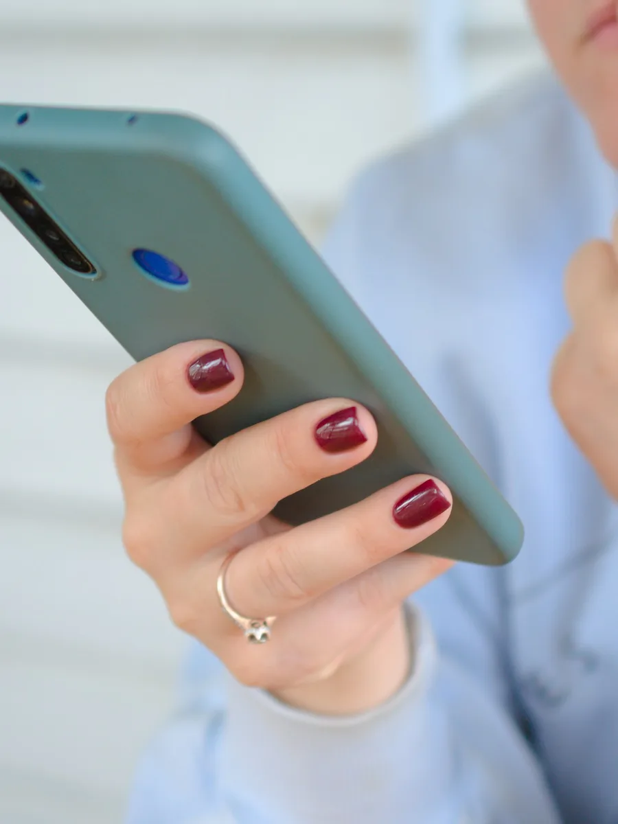 Une main aux ongles vernis tient un smartphone à coque turquoise