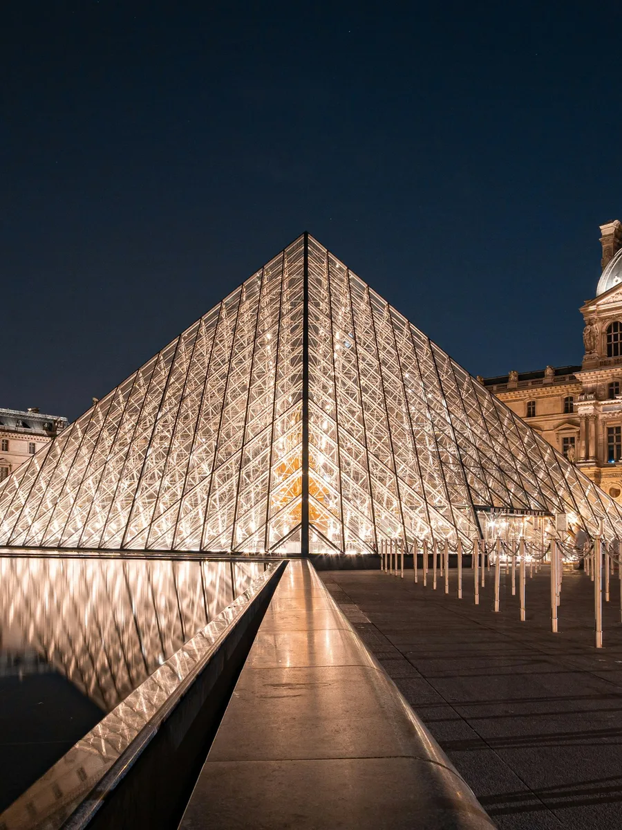 La pyramide du Louvre illuminée la nuit, reflétée dans un bassin