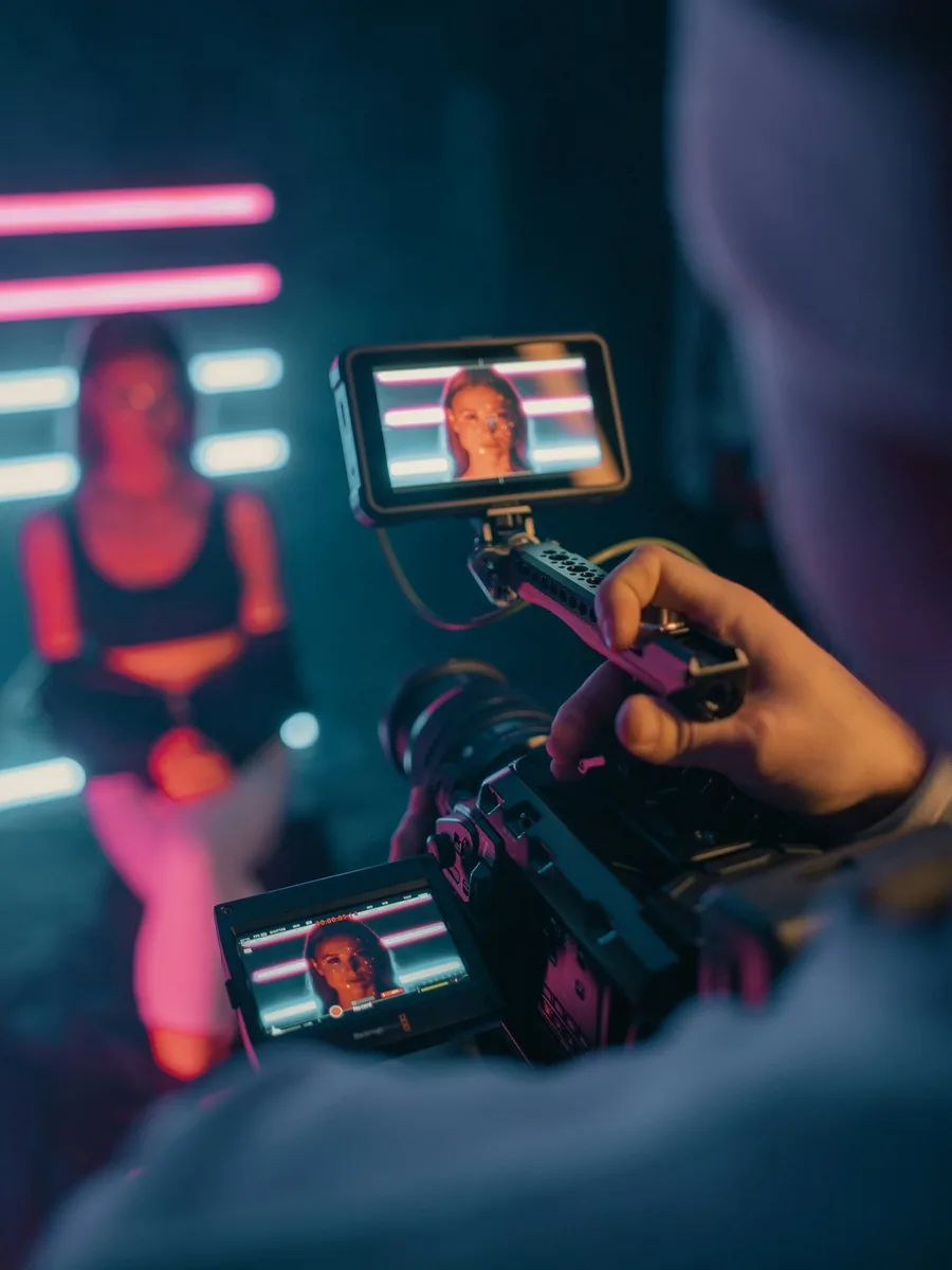 Une main tient un smartphone monté sur une poignée, qui filme une personne devant des néons roses