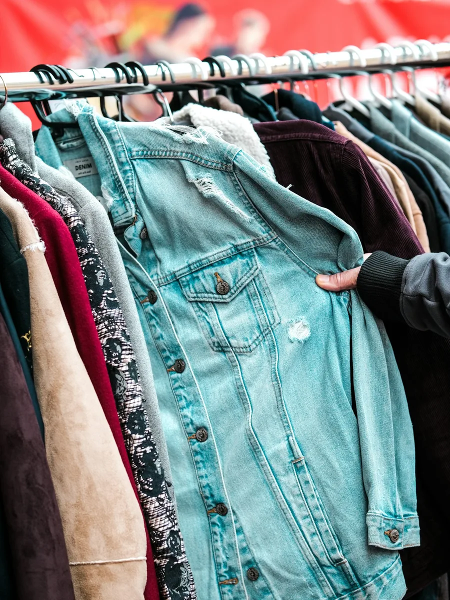 Des vestes et chemises d'occasion serrées sur un portant, une main en saisit une