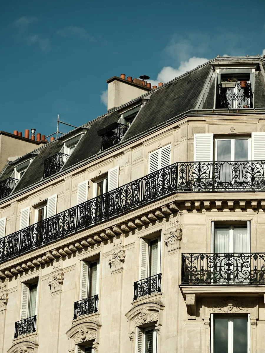 Façade d'un immeuble haussmannien à Paris, balcons en fer forgé et toits en zinc sous un ciel bleu