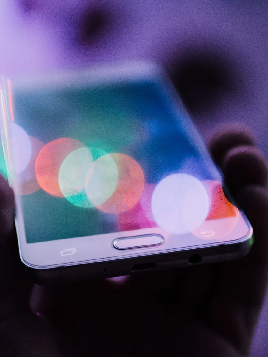 Une main tient un smartphone allumé sur un fond de lumières floues