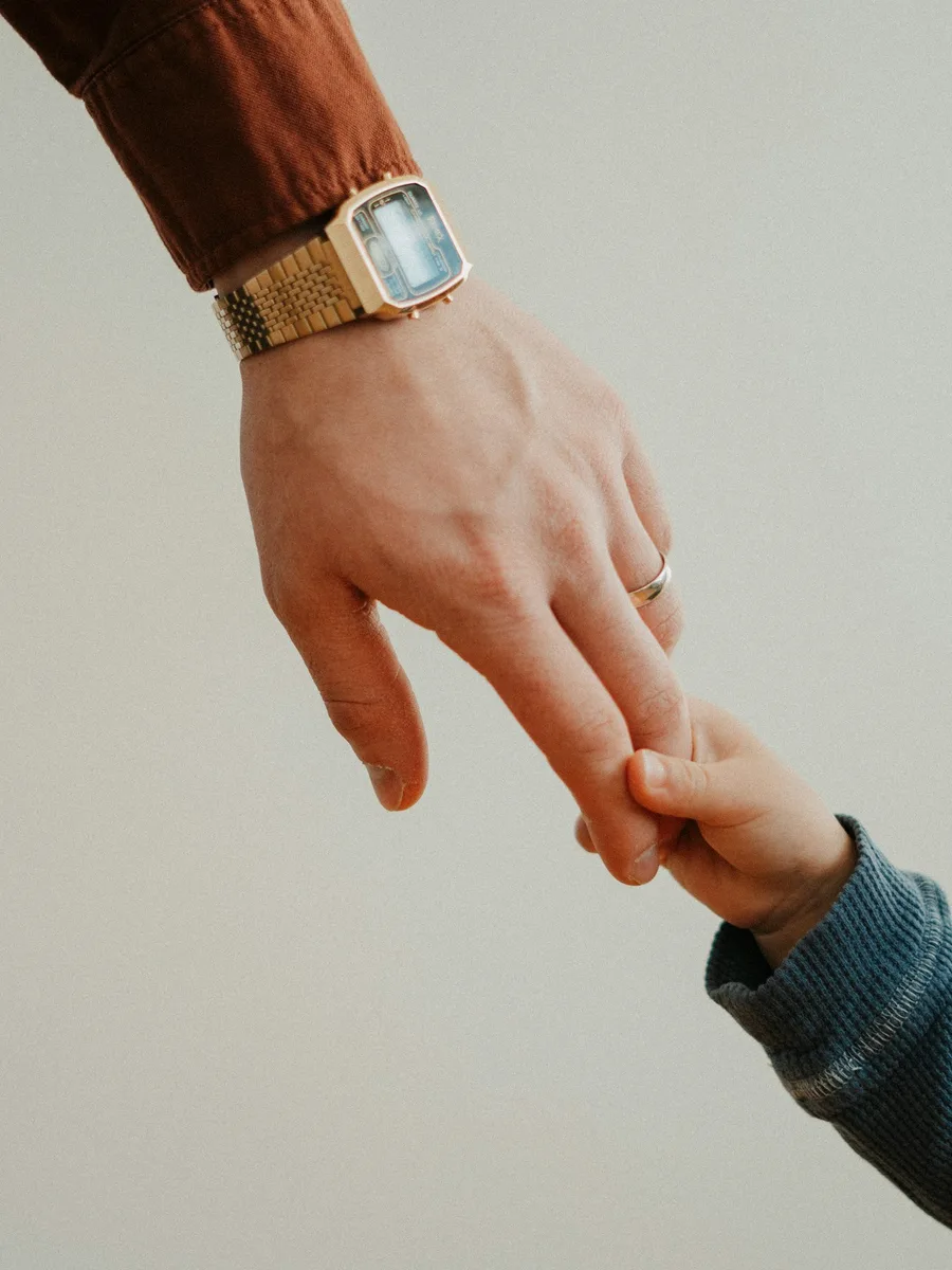 La main d'un adulte portant une montre tient le doigt d'un jeune enfant