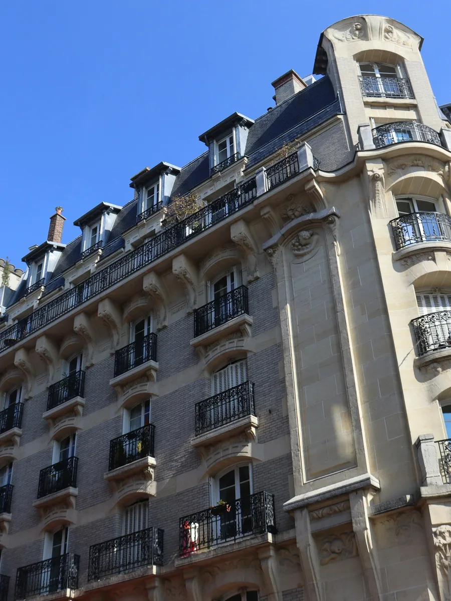 Façade d'un immeuble parisien en pierre, avec balcons en fer forgé et toit en zinc, sous un ciel bleu