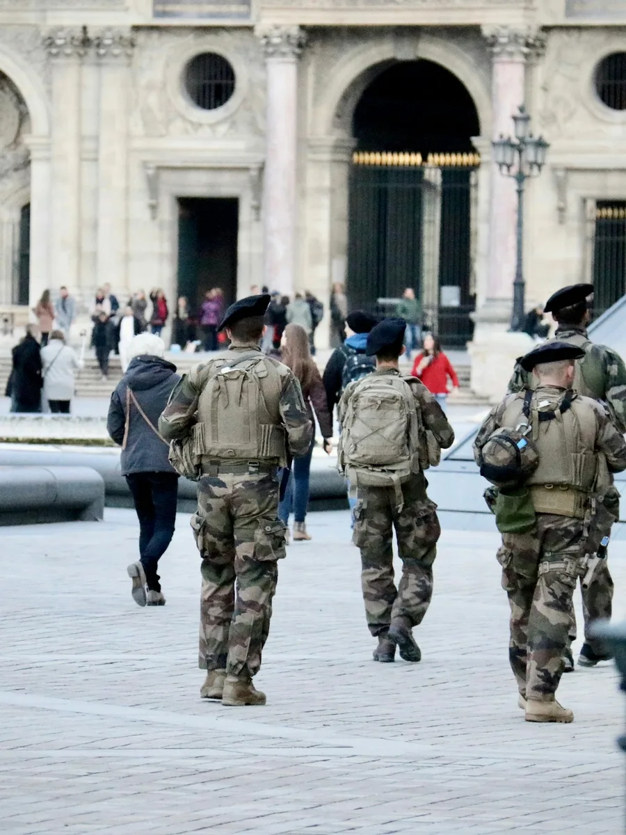 Des militaires en treillis, sac au dos et fusil, patrouillent parmi les passants dans une cour du Louvre à Paris