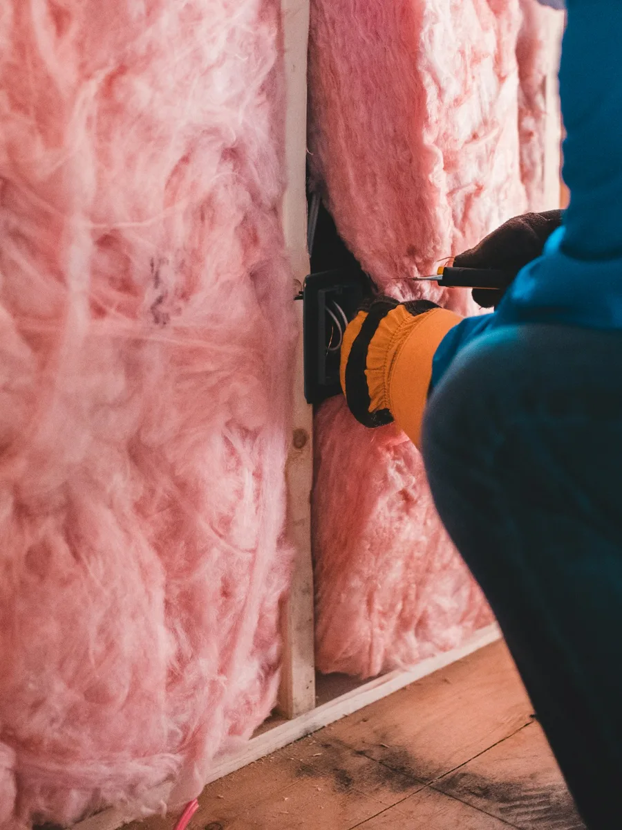 Un ouvrier pose du câblage dans un mur rempli de laine de verre rose.