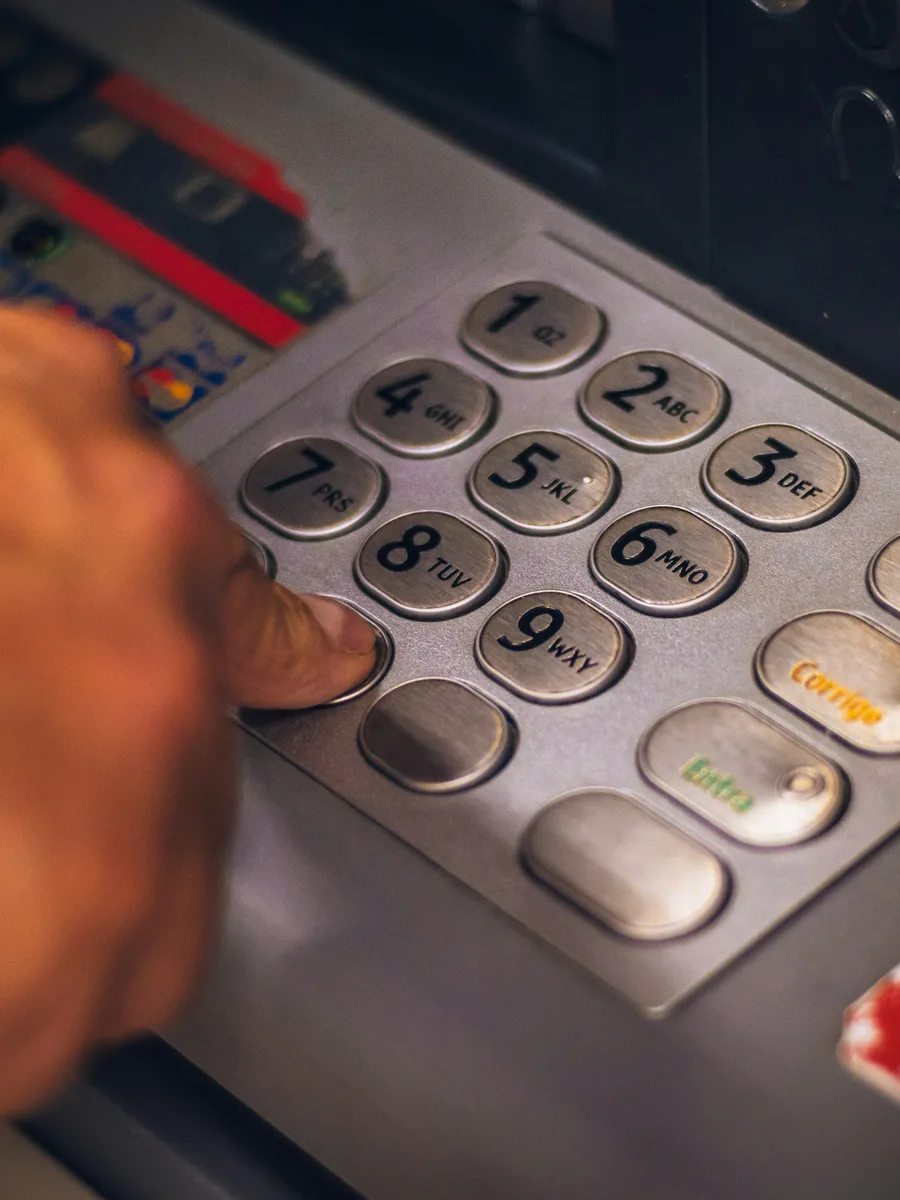 Une main tape un code sur le clavier métallique d'un distributeur de billets
