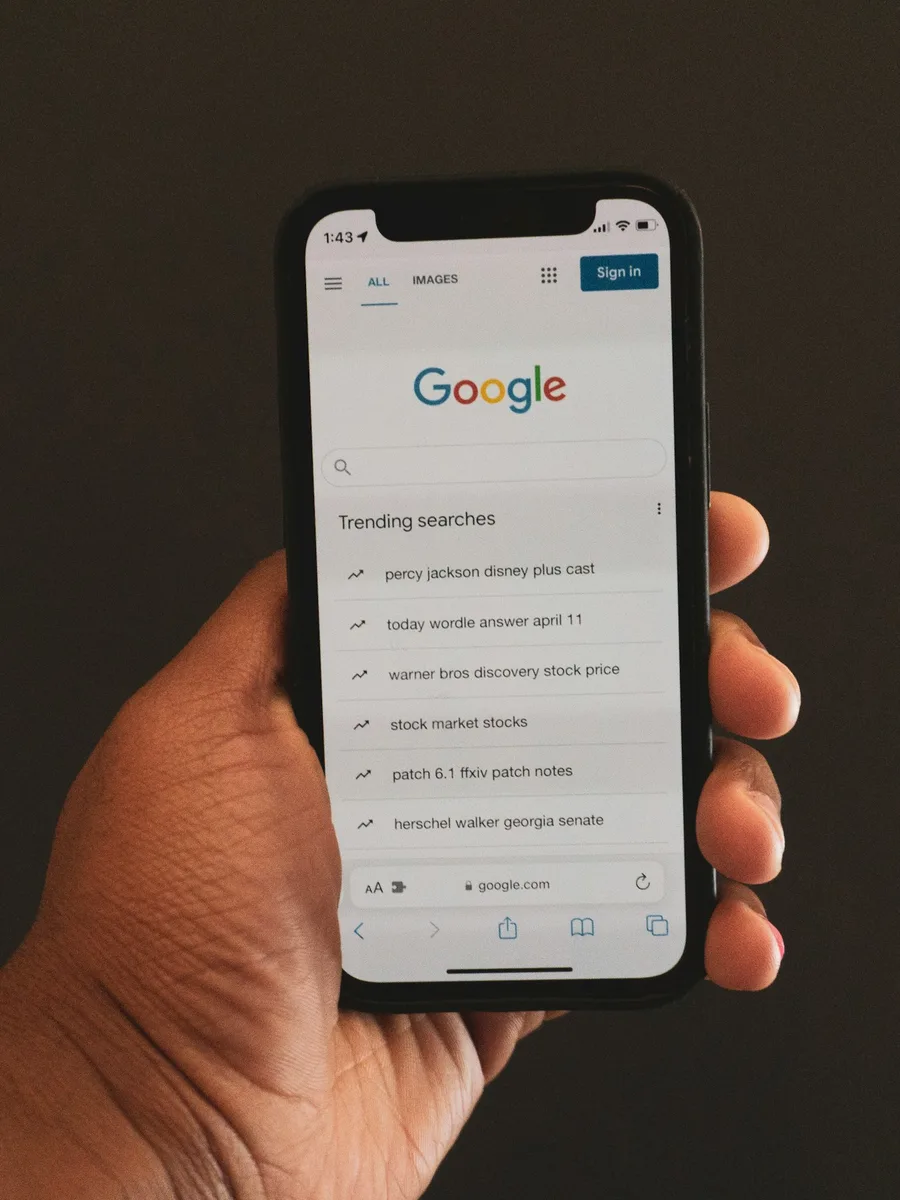 Une main tient un smartphone affichant la page d'accueil de Google.
