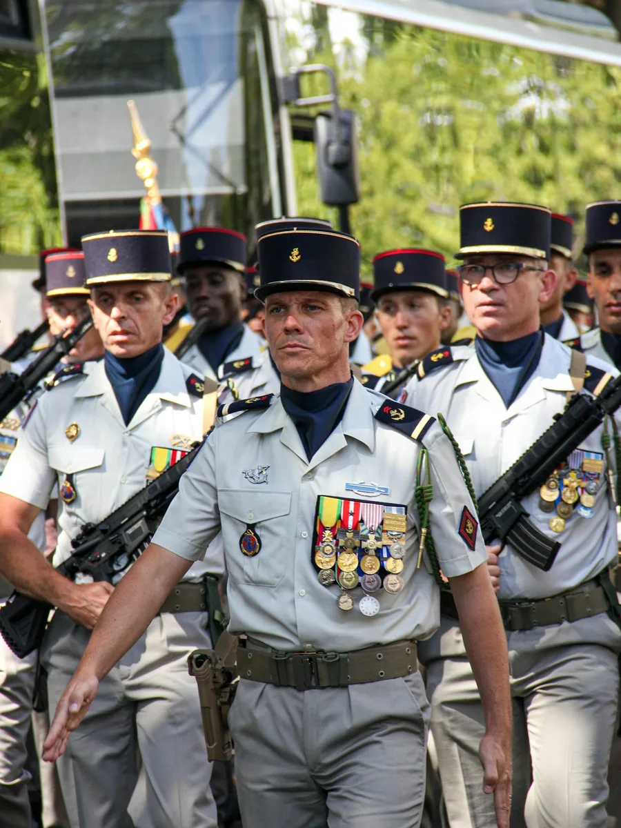 Militaires français en tenue de défilé, képi sur la tête et arme à l'épaule, dans une rue de Paris.