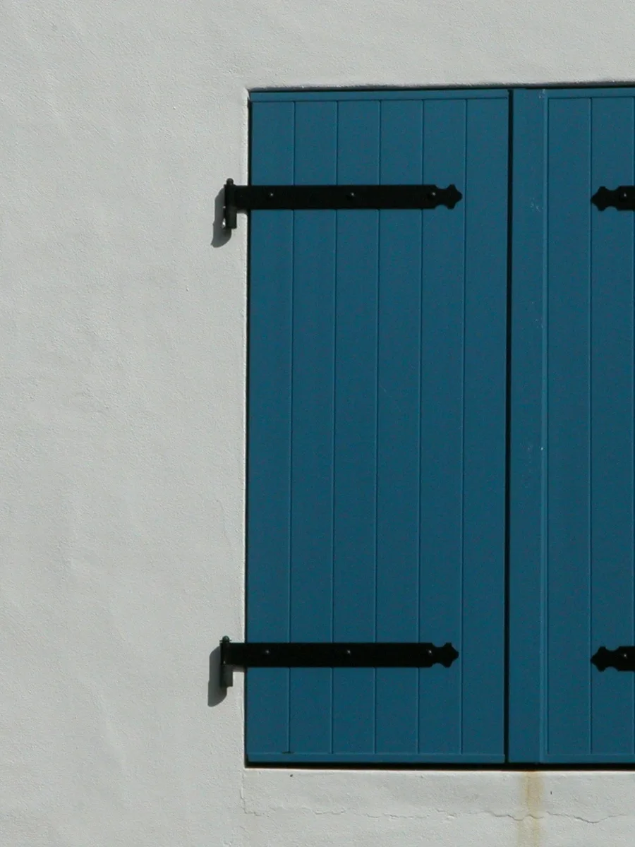 Des volets en bois bleus fermés sur un mur blanc