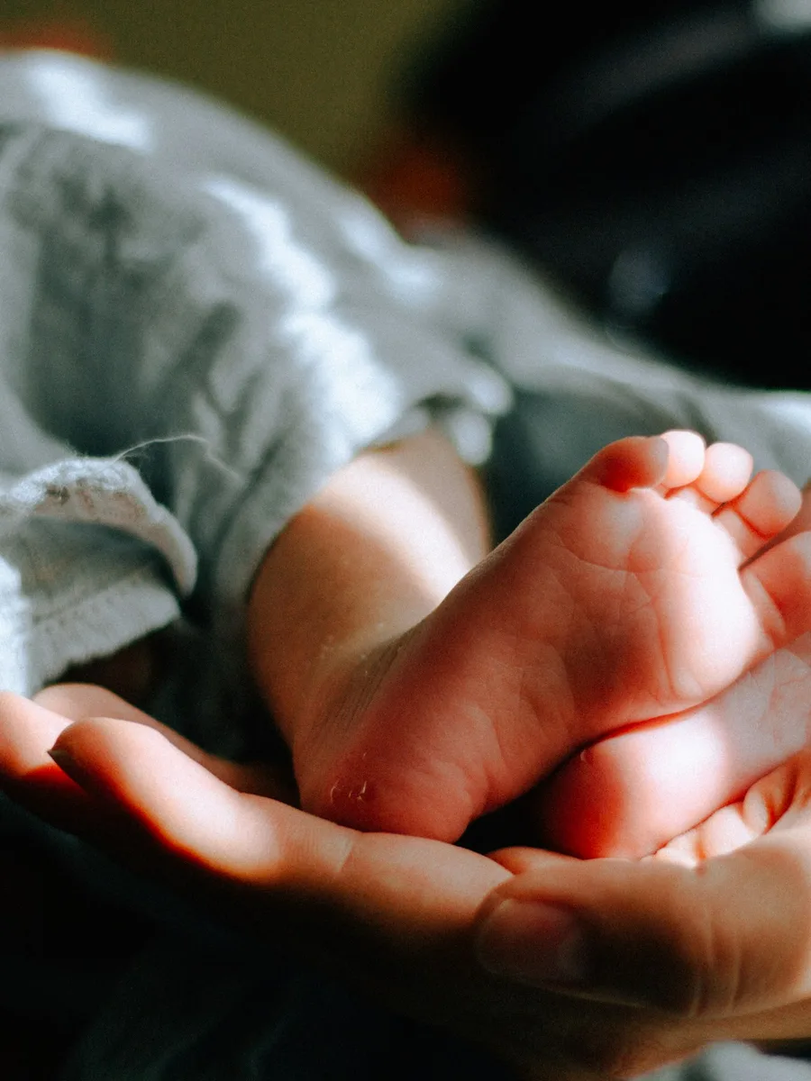 Une main d'adulte tient délicatement les pieds d'un nouveau-né.