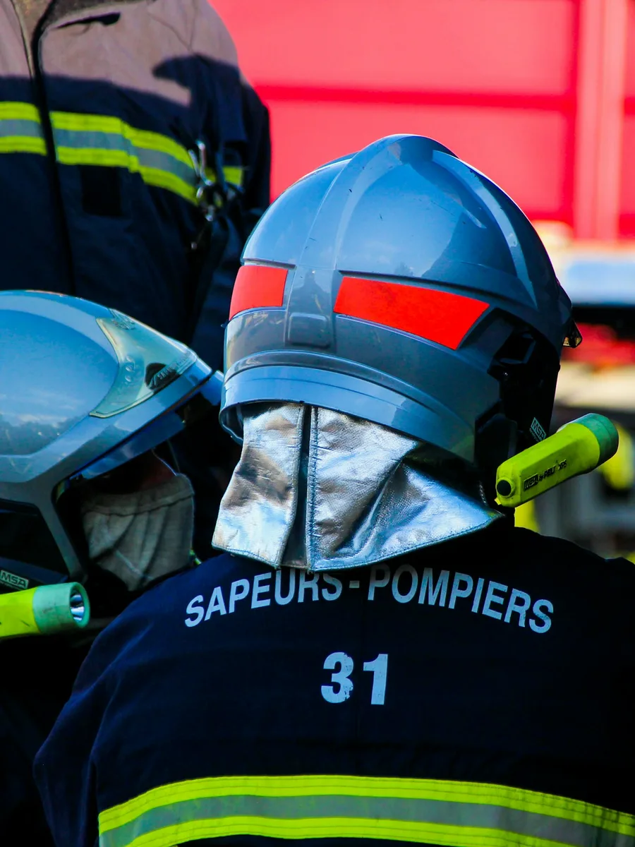 Deux sapeurs-pompiers casqués, vus de dos, devant un camion rouge lors d'une intervention