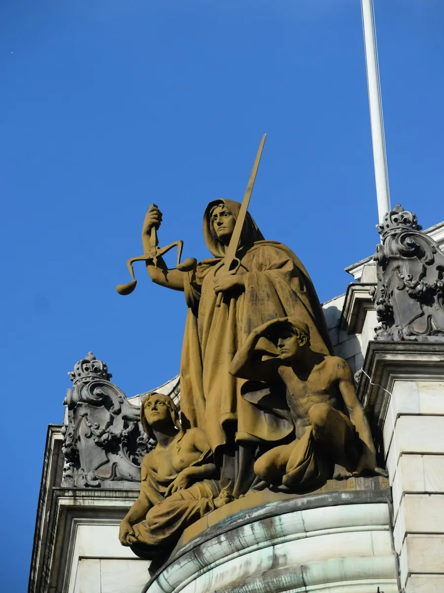 Statue de la Justice tenant une balance et une épée au sommet d'un bâtiment, sous un ciel bleu