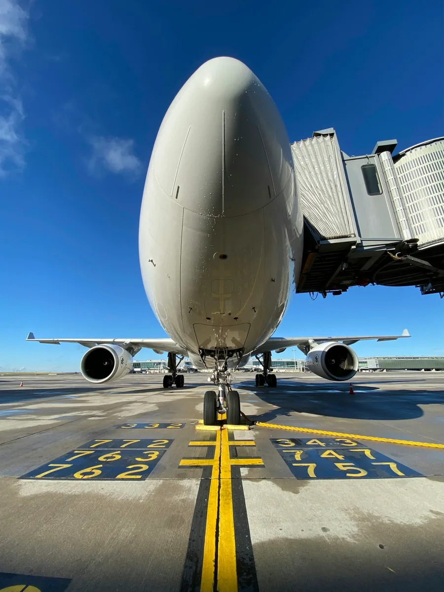 Avion de ligne Airbus A330 stationné face à une passerelle d’embarquement à l’aéroport Paris-Charles-de-Gaulle, vu de face sous un ciel bleu.
