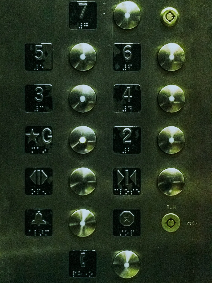 Gros plan sur le panneau de commande métallique d’un ascenseur, avec ses boutons d’étage numérotés.