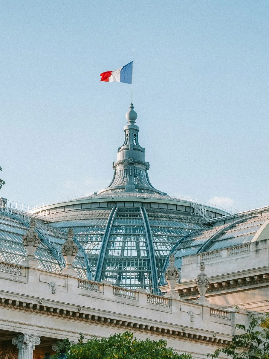 Le dôme vitré du Grand Palais, à Paris, surmonté d'un drapeau français sous un ciel bleu