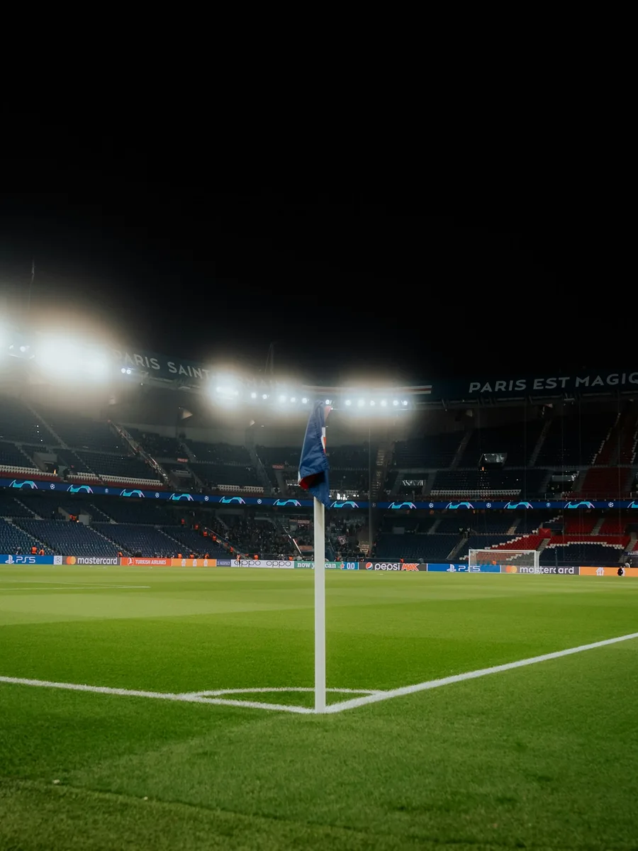 Un drapeau de corner au premier plan sur la pelouse du Parc des Princes, de nuit, devant les tribunes éclairées