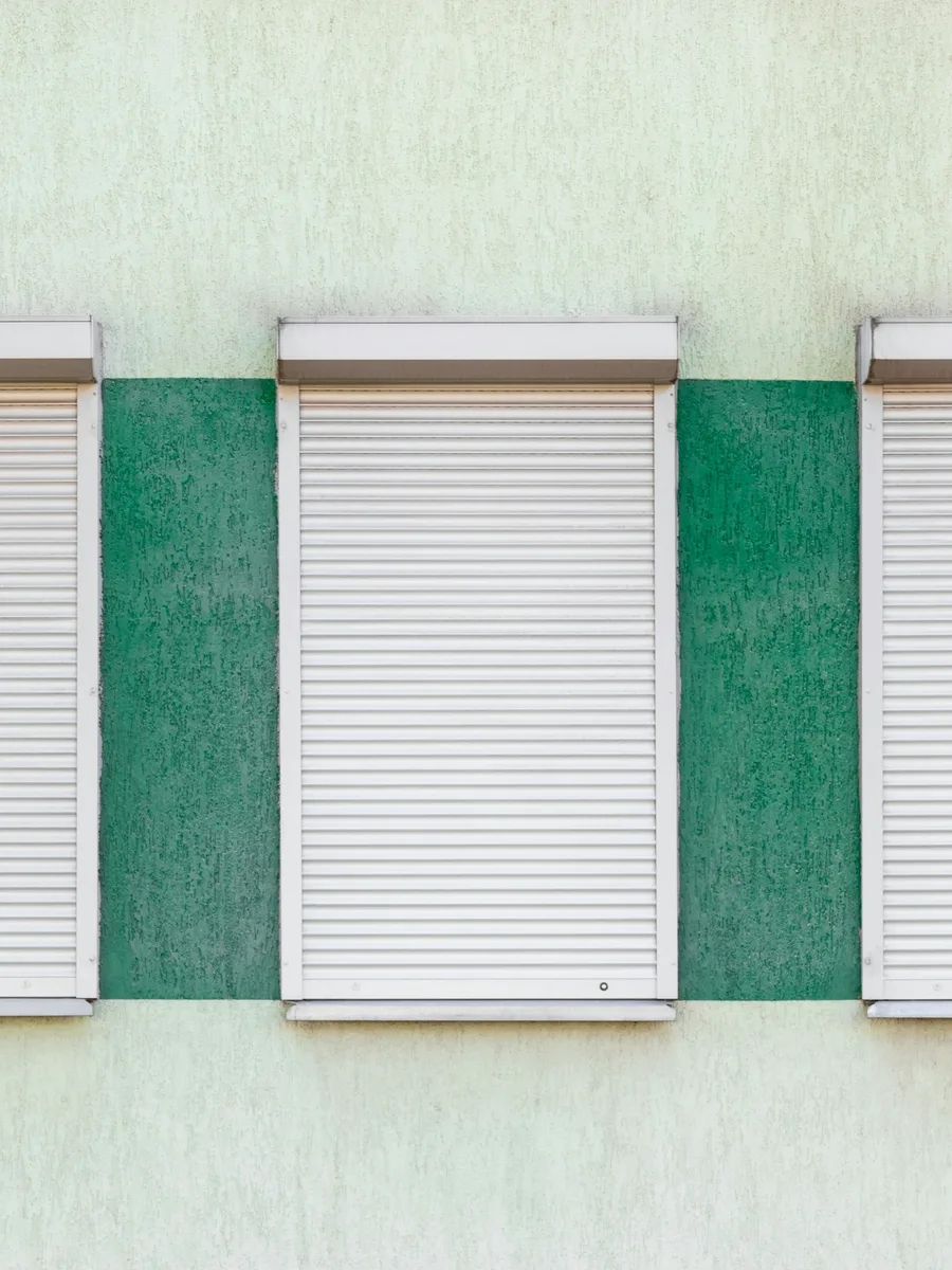 Des volets roulants fermés sur une façade peinte en vert et blanc