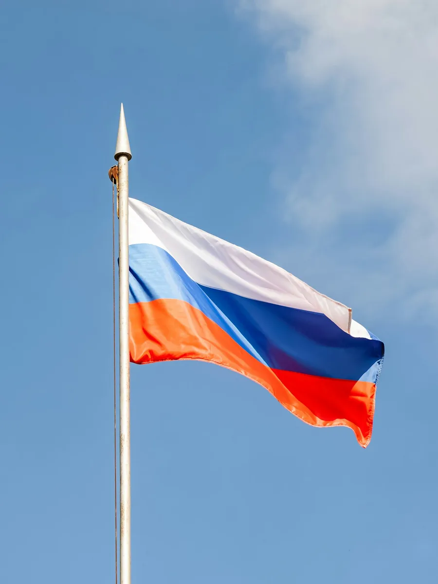 Le drapeau russe blanc, bleu et rouge flotte au sommet d'un mât sous un ciel bleu.