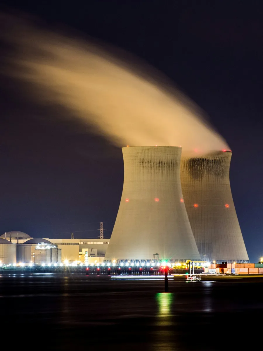 Deux tours de refroidissement d'une centrale nucléaire rejetant de la vapeur la nuit, au bord d'un fleuve