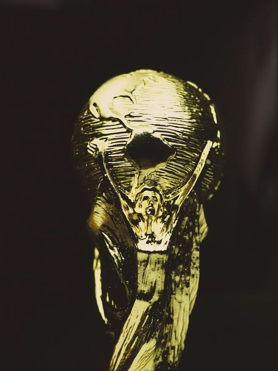 Réplique dorée du trophée de la Coupe du monde de football, avec son globe, sur fond sombre.