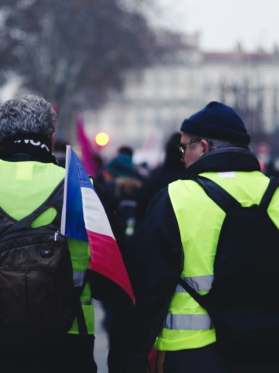 Deux manifestants de dos portant des gilets jaunes, au milieu d'un rassemblement dans une rue
