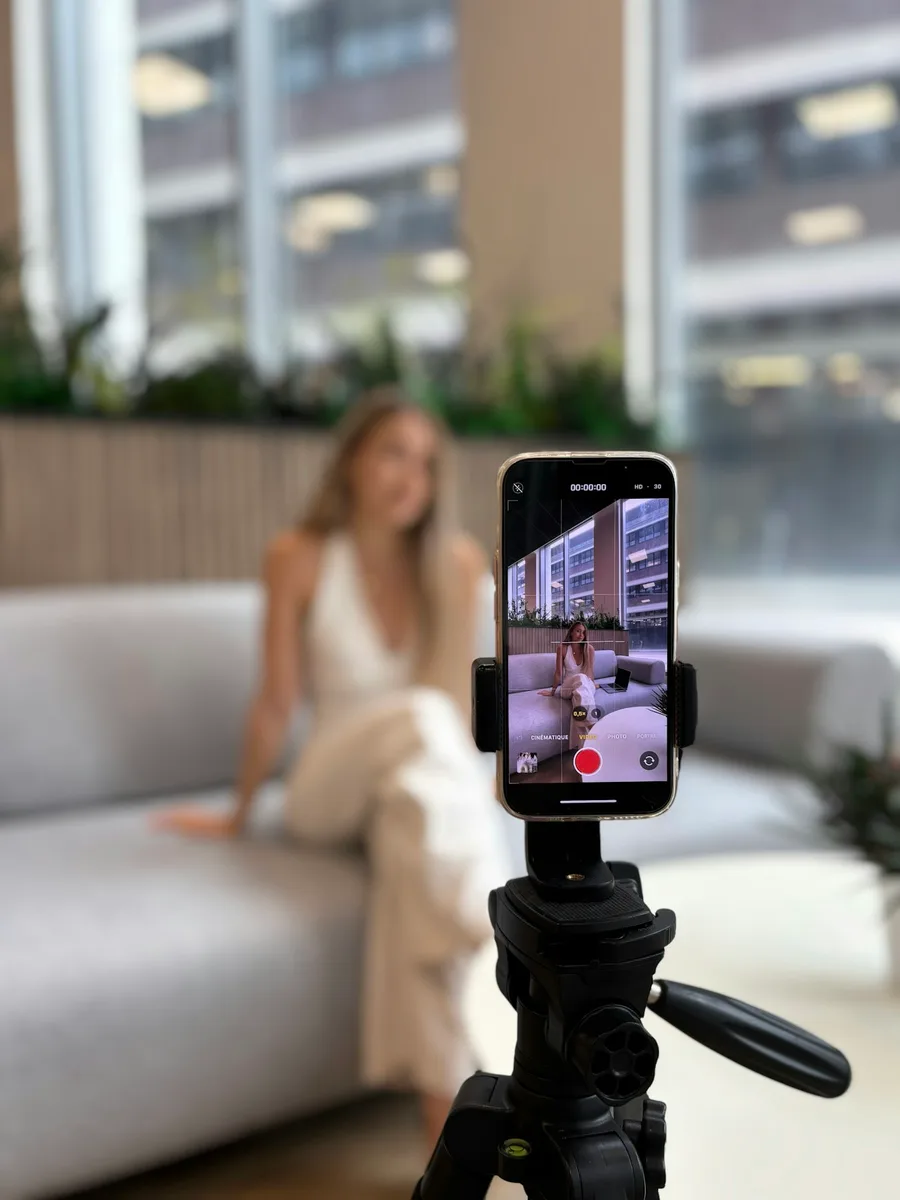 Un smartphone monté sur trépied filme une jeune femme assise en arrière-plan