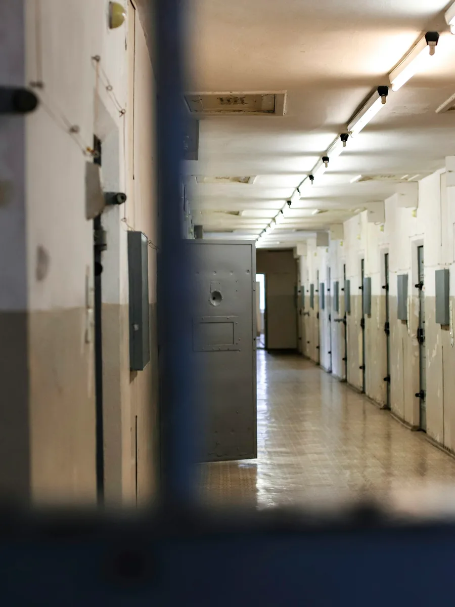 Un couloir de détention bordé de portes de cellules, vu à travers des barreaux