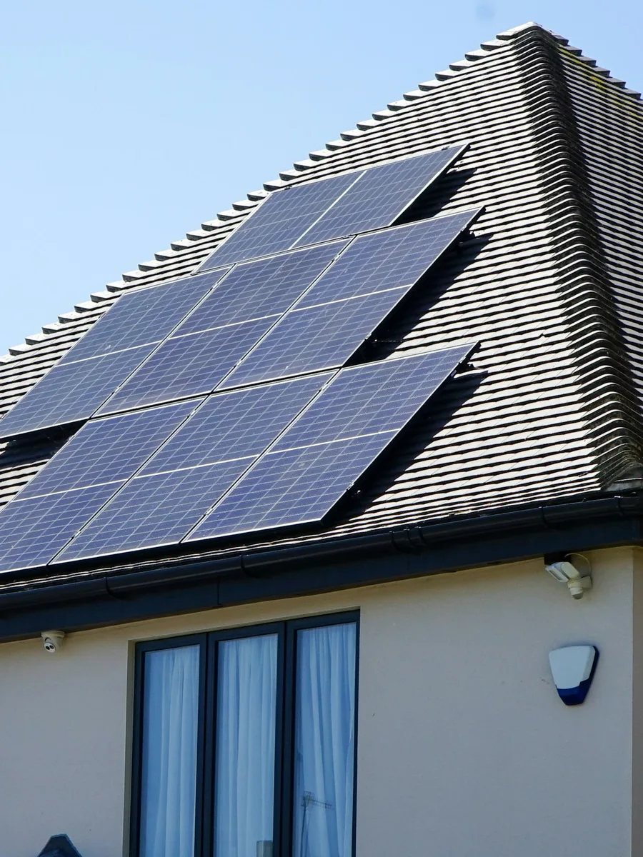 Des panneaux solaires installés sur le toit en tuiles sombres d'une maison, sous un ciel bleu