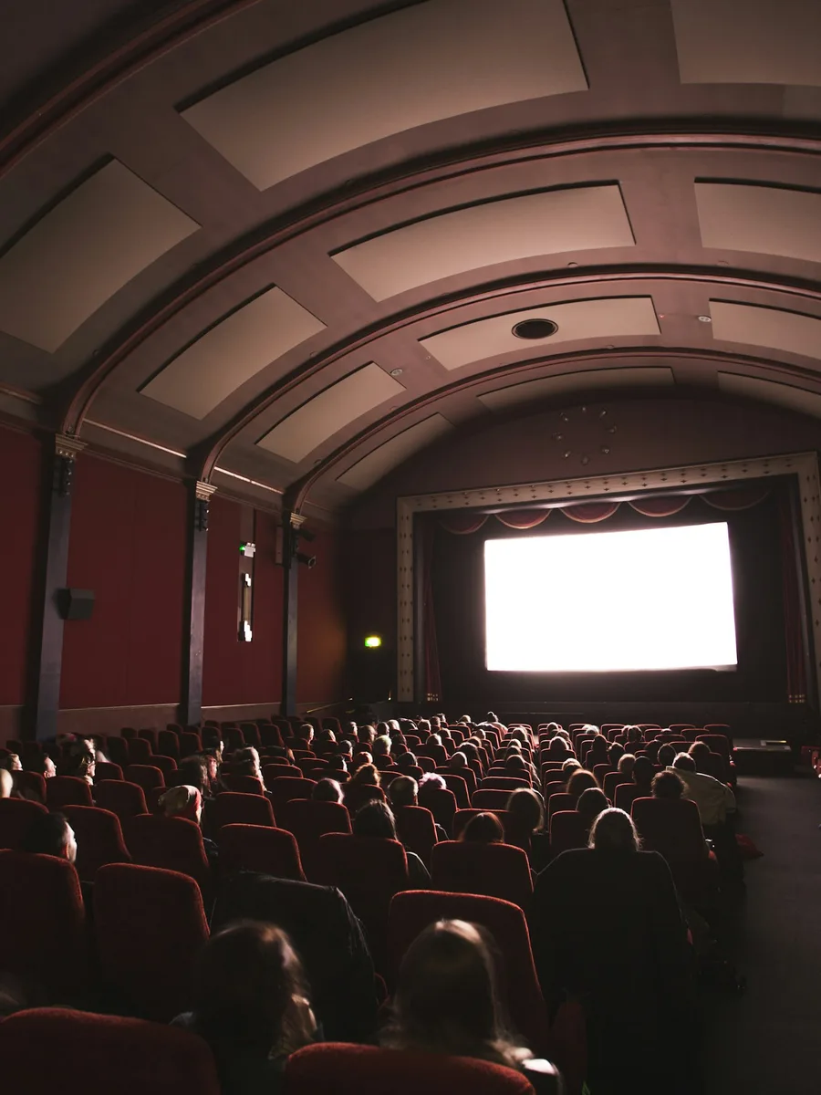 Salle de cinéma plongée dans le noir, spectateurs face à l'écran