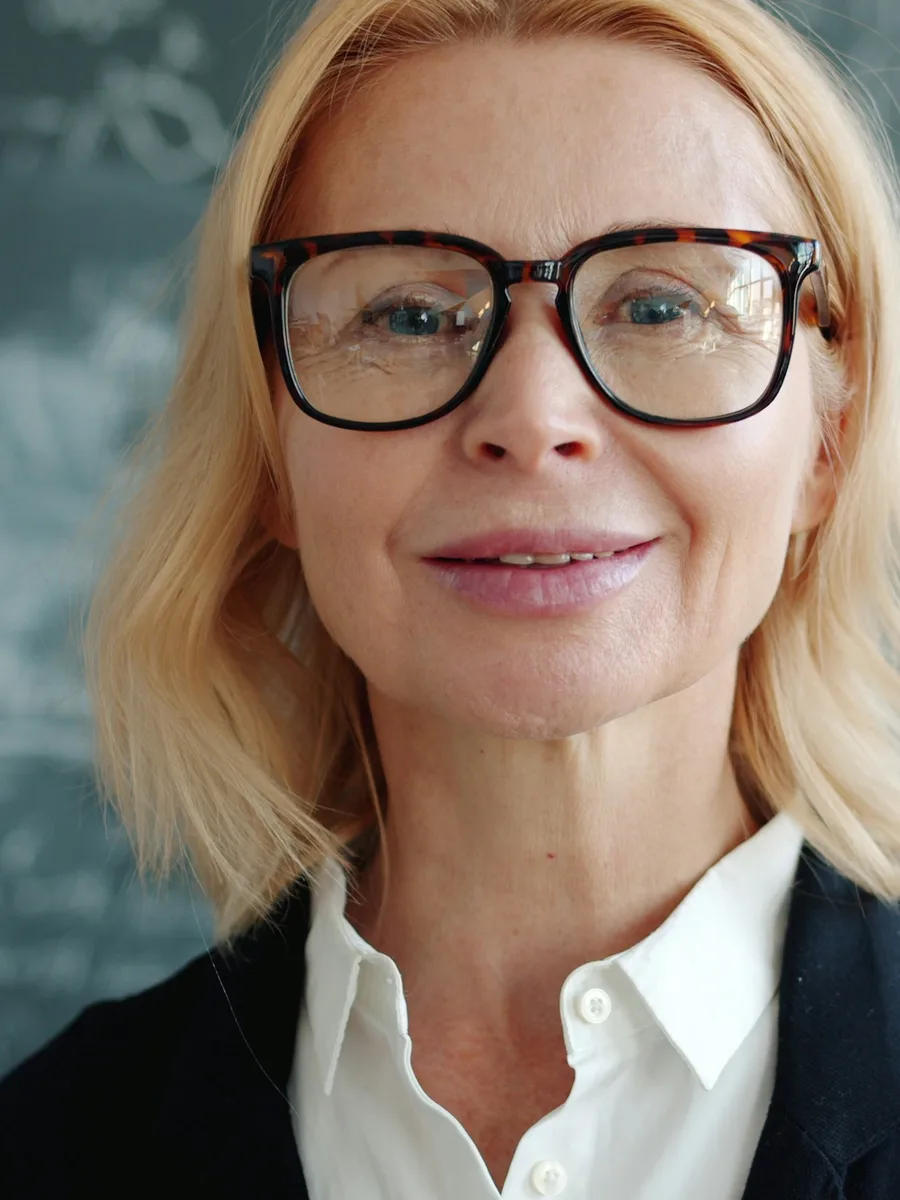 Portrait d'une enseignante à lunettes, souriante, devant un tableau noir