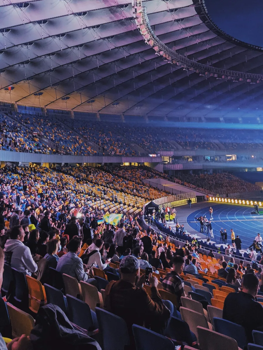 Tribunes d'un grand stade de football remplies de spectateurs, en soirée, sous la toiture éclairée