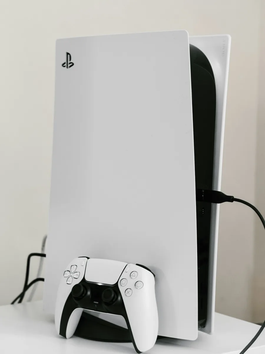 Une console PlayStation 5 blanche posée debout, avec sa manette.