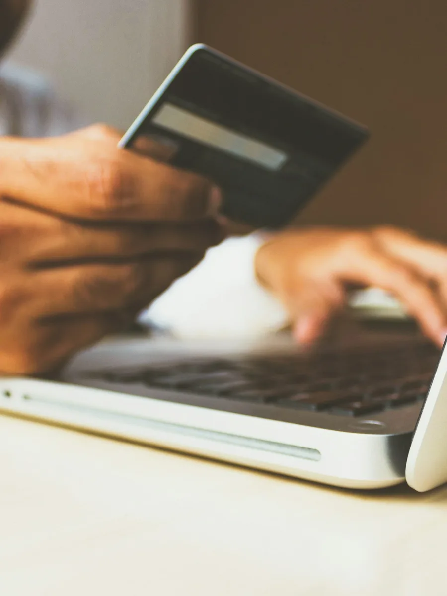 Une personne tient une carte bancaire devant le clavier d'un ordinateur portable